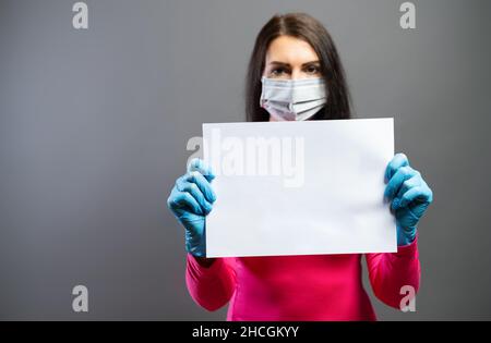 Frau in medizinischer Maske und Handschuhen, die leeres leeres Papier als Zeichen des Protests in ihren Händen zeigt. Konzentrieren Sie sich auf ein Stück Papier. Verhindern Sie, dass andere Corona COVI Stockfoto