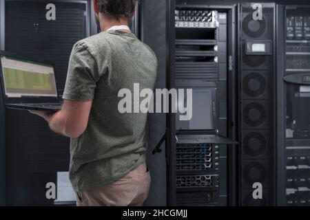 Rechenzentrumsingenieur, der die Einrichtung eines Spezialisten für Laptop-Computer im Serverraum verwendet, mit einem männlichen Systemadministrator, der mit dem Datenschutznetzwerk für arbeitet Stockfoto