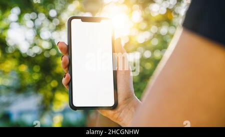 Mockup Bild von Frauen Hände halten schwarzes Smartphone mit weißem leeren Bildschirm auf einem im Park Stockfoto