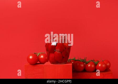 Hausgemachte Tomatensauce in einem Glas auf Holzpodest, Tomaten auf rotem Backgroud Stockfoto
