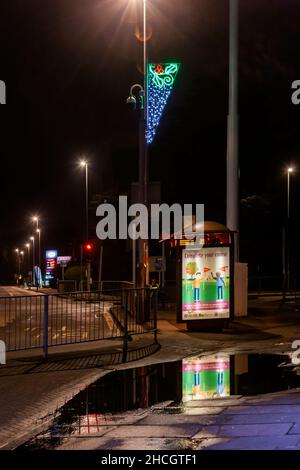 Bushaltestelle mit Neon-Schild, das sich in einer Pfütze auf der Wellingborough Road, Northampton, England, Großbritannien, widerspiegelt Stockfoto