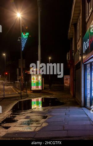 Bushaltestelle mit Neon-Schild, das sich in einer Pfütze auf der Wellingborough Road, Northampton, England, Großbritannien, widerspiegelt Stockfoto