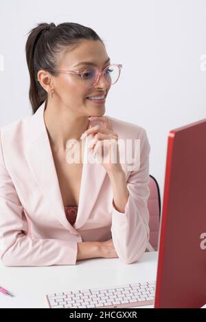 England, Großbritannien. 2021. Attraktive weibliche Büroangestellte, die eine Brille trägt und auf den Computerbildschirm schaut. Stockfoto