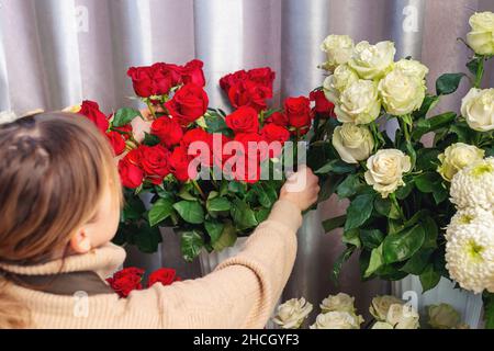 Floristik, Geschäft, Dekoration Konzept. Blumenhändler, der Rosenblumen arrangiert. Rückansicht einer Verkäuferin. Florist wählt Blumen für die Herstellung von Bouquet Stockfoto