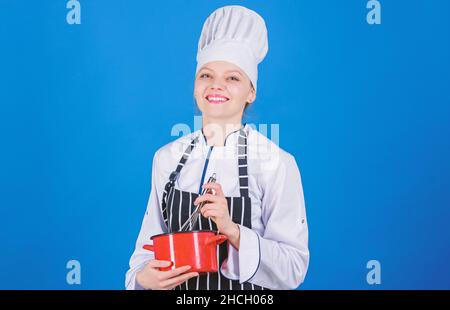 Frau professionelle Koch halten Schneebesen und Topf. Peitschend wie ein Profi. Mädchen in der Schürze peitschende Eier oder Creme. Beginnen Sie langsam mit Schlagsahne oder Schlagsahne Stockfoto