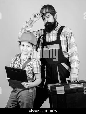 Vater und Tochter in der Werkstatt. Werkstatt in Uniform. Techniker. Bärtiger Mann mit kleinem Mädchen. Bauarbeiterassistent. Baumeister oder Zimmermann Stockfoto