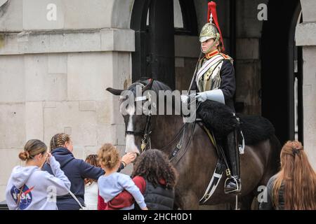 Touristen um eine junge Soldatin, bestiegen auf dem Pferderücken, Blues und Royals Mitglied der Household Cavalry bei der Horse Guards Parade, London, Großbritannien Stockfoto