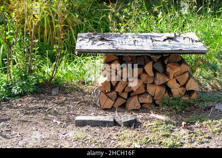 Lagerung von Brennholz im Freien - überdachte Holzstämme gestapelt. Feuerholz Lager auf dem Land. Brennholz für den Winter. Stockfoto