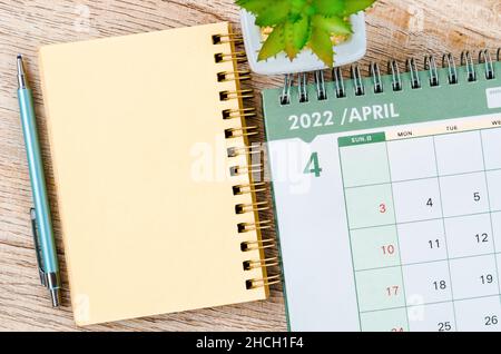 April 2022 Tischkalender und Tagebuch mit kleiner Pflanze auf Holzhintergrund. Stockfoto