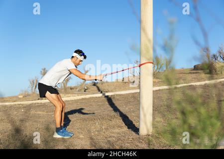 Der junge Kaukasusmann trainiert mit einem Gummiband im Park Stockfoto