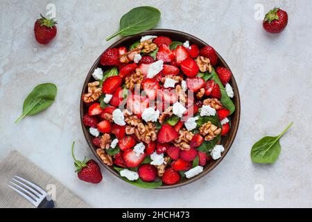Flatlay eines Tellers mit hausgemachtem frischen Salat aus Babyspinatblättern, geschnittenen Erdbeeren, Walnüssen, Feta-Käse und einem leichten Vinaigrette-Dressing. Stockfoto