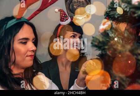 Zwei schöne glückliche junge Frauen schmücken weihnachtsbaum am heiligabend Stockfoto