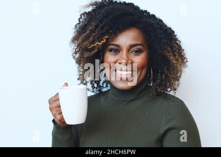 Lächelnde Erwachsene afroamerikanische Frau mit lockigen Haaren und einer weißen Tasse Stockfoto