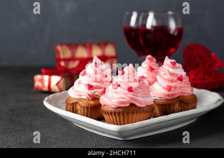 Hausgemachte Cupcakes mit Creme- und herzförmigen Prise zum Valentinstag auf dunkelgrauem Hintergrund Stockfoto