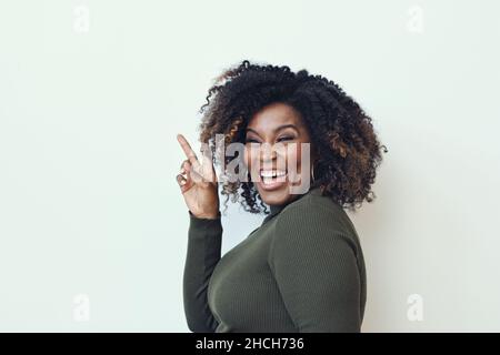 Seitenansicht einer fröhlichen, lockigen Frau mit Friedenszeichen vor weißem Hintergrund Stockfoto