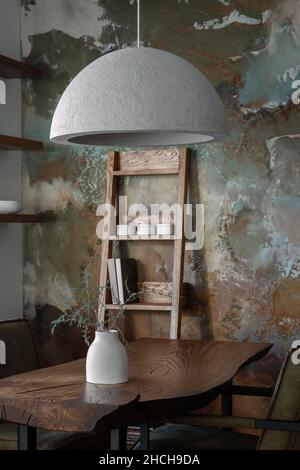 Stilvolle waldreiche Einrichtung des Esszimmers mit massivem Eichenholztisch, Eichenregal und grünen Stühlen, Betonvase, eleganten Zement-Accessoires Stockfoto