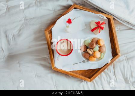 Draufsicht hausgemachtes Valentinstag-Frühstück im Bett für Liebhaber. Eine Tasse Kaffee, Makronen, herzförmige Geschenkbox mit rotem Band und leere Karte für wi Stockfoto