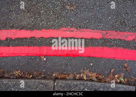 Nahaufnahme der doppelten roten Linien Straßenmarkierungen, die auf eine rote Route hinweisen und darauf hinweisen, dass zu jeder Zeit und an allen Tagen Regeln und Vorschriften gelten Stockfoto