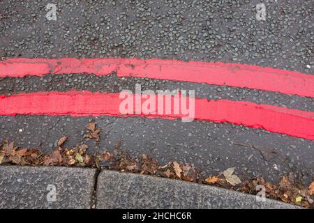 Nahaufnahme der doppelten roten Linien Straßenmarkierungen, die auf eine rote Route hinweisen und darauf hinweisen, dass zu jeder Zeit und an allen Tagen Regeln und Vorschriften gelten Stockfoto