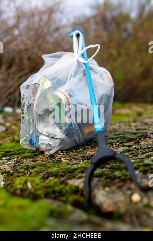 Ein Müllsammler und ein voller Müllbeutel, der von einem Strandreinigungsgerät gesammelt wurde, sammeln weggeworfenen Müll und Müll. Wurfpflücken, Umgebung Stockfoto