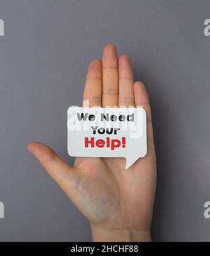 Das Mädchen hat eine Visitenkarte mit dem Text in der Hand, wir brauchen deine Hilfe Stockfoto