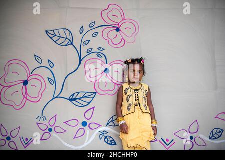 Rajshahi, Bangladesch. 25th Dez 2021. Ein Kind posiert für ein Foto vor ihrem gemalten Haus in Rajshahi. Der Stamm der Santal ist eine ethnische Gruppe, die in Ostindien beheimatet ist. Santals sind in Bezug auf die Bevölkerung der größte Stamm im Bundesstaat Jharkhand in Indien und werden auch in den Staaten Assam, Tripura, Bihar, Odisha und Westbengalen gefunden. Sie sind die größte ethnische Minderheit in der Rajshahi-Division und der Rangpur-Division im Norden Bangladeschs. Kredit: SOPA Images Limited/Alamy Live Nachrichten Stockfoto