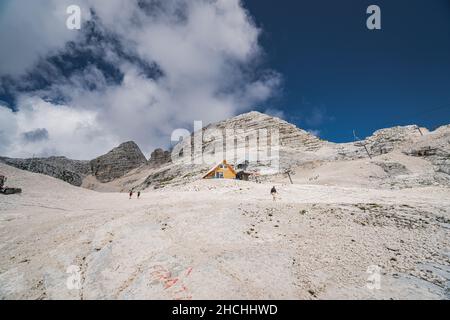 Eine Gruppe von Leuten, die an einem sonnigen Tag auf einem verschneiten Berg mit einem kleinen Häuschen im Hintergrund Ski fahren Stockfoto
