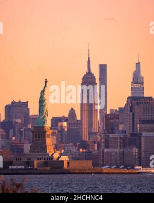 New York, NY - USA -26. Dez 2021: Vertikale Sicht am frühen Morgen auf die Freiheitsstatue im New Yorker Hafen, mit dem Empire State Building und dem Stockfoto