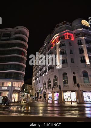 Nachtansicht der modernen Gebäude in der Innenstadt von Cannes, Französische Riviera, Frankreich am Abend mit beleuchteten Schaufenstern von Dior und Prada. Stockfoto