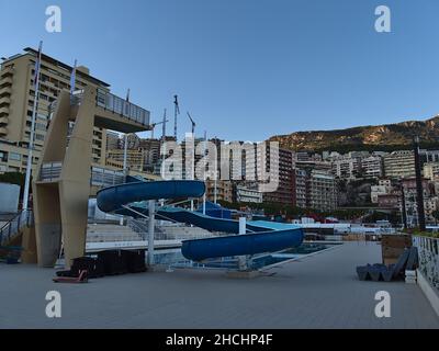 Blaue Wasserrutsche und Sprungbrett im Rainier III Nautical Stadium in der Innenstadt von Monaco am Abend mit Wohnhochhäusern. Stockfoto