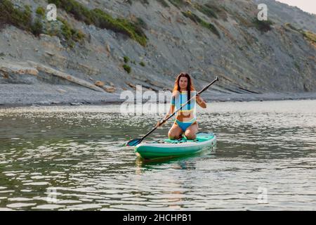 4. August 2021. Anapa, Russland. Sportliche Frau, die auf dem Stand Up Paddle Board in Black Sea schwimmt. Frau Urlaub auf Red paddel supboard im Meer. Stockfoto