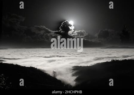 Berglandschaft bei Nacht. Der Mond, der aus den Wolken aufsteigt, erhellt das Meer von ​​fog auf der Ebene. Stockfoto