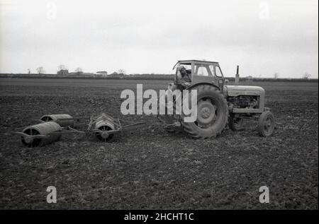 1960s, historisch, ein Landwirt auf seinem Traktor, ein Ferguson „Super Major“, stationär auf einem Feld, mit Wetterkabine und Außenwalzen, England, Großbritannien. Henry George „Harry“ Ferguson war ein in Irland geborener britischer Ingenieur und Erfinder, bekannt für seine Entwicklung des modernen landwirtschaftlichen Traktors, insbesondere des „Ferguson-Systems“, einer hydraulischen Dreipunktanhängung oder eines Befestigungssystems am Heck des Traktors für das angeschlossene Anbaugerät. Er kam zu einer Vereinbarung mit Henry Ford, und 1939 wurde der erste Ford-Ferguson-Traktor auf den Markt gebracht. Stockfoto