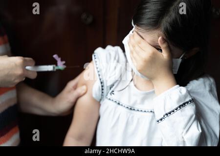 Kleines Mädchen bedeckt das Gesicht mit der Hand, die Angst hat, einen Impfstoff zu bekommen. Covid-19, Coronavirus-Kinderimpfung, Angstkonzepte Stockfoto