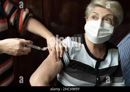 Ältere Frau mit OP-Maske erhält Covid-19-Impfstoff. Chirurg mit Spritze, die eine ältere Dame mit bedeckenden Gesicht beschossen hat Stockfoto