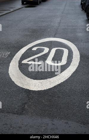 Straßenschild 20 Meilen pro Stunde. 20 in weißer Straßenfarbe gestrichen, mit einem weißen Kreis um ihn herum, auf einer schwarz-grauen gepflasterten Straße. Stockfoto