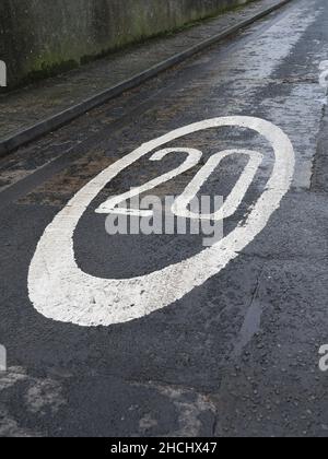 Straßenschild 20 Meilen pro Stunde. 20 in weißer Straßenfarbe gestrichen, mit einem weißen Kreis um ihn herum, auf einer schwarz-grauen gepflasterten Straße. Stockfoto