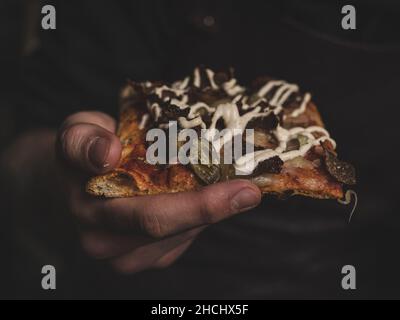 Nahaufnahme einer Hand mit einem Stück Pizza Stockfoto