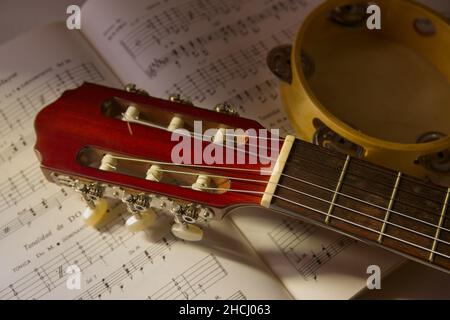 Bild einer klassischen spanischen Gitarre neben einem Tamburin über eine Partitur, um das Gitarrenspiel zu lernen. Stockfoto