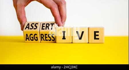 Aggressives oder durchsetzungskräftiger Symbol. Geschäftsmann dreht Holzwürfel, ändert das Wort aggressiv zu durchsetzungsfähig. Schöner weißer Hintergrund, Kopierbereich. Busi Stockfoto