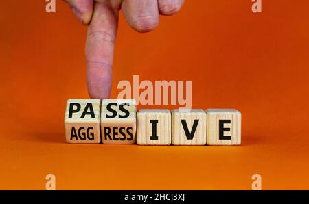 Passives oder aggressives Symbol. Geschäftsmann dreht Holzwürfel und ändert das Wort passiv in aggressiv. Schöner orangefarbener Hintergrund, Kopierbereich. Busi Stockfoto