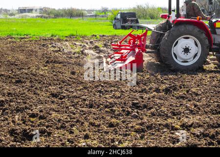 Ein Traktor pflügt das Land auf einem Gartengrundstück an einem Frühlingstag. Landwirtschaft und Agronomie. Stockfoto