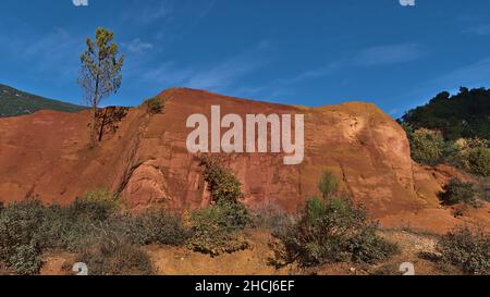 Atemberaubende Aussicht auf orange und rot gefärbte ockerfarbene Felsen in Colorado Provenzal mit grünen Büschen und Bäumen in der Nähe von Rustrel im Luberon-Tal, Provence, Frankreich. Stockfoto