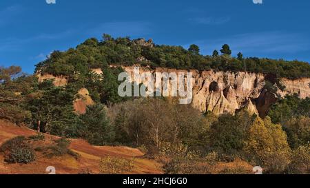 Atemberaubender Blick auf die bunten ockerfarbenen Felsformationen mit orangefarbenen und gelben Farben in der Provenzalkirche Colorado in der Nähe von Rustrel in der Provence, Frankreich, an sonnigen Tagen. Stockfoto