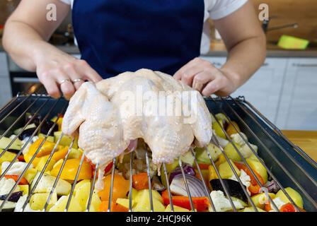 Der Koch legt das rohe Huhn auf ein Backblech mit Gemüse. Der Prozess des Kochens gegrilltes Huhn im Ofen mit gebackenem Gemüse zu Hause. Stockfoto