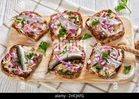 Eingelegte Sprotte offene Sandwiches mit Butter und roten Zwiebeln auf Roggenbrotscheiben auf Holzbrett auf einem weißen Tisch mit Struktur Stockfoto