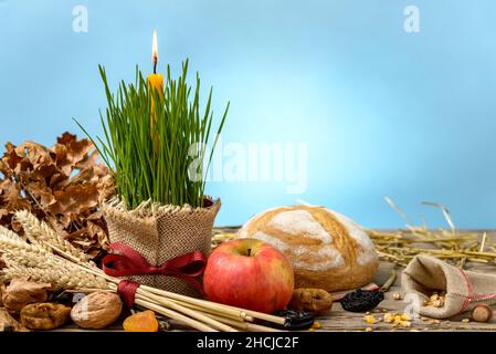 Traditionelles Essen für den orthodoxen Heiligabend. Yule log oder badnjak, die Äpfel, das Brot, die Getreide, die getrockneten Früchte und die brennende Kerze im grünen Weizen auf dem Holz Stockfoto