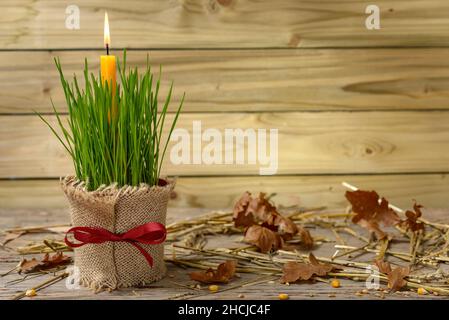 Grüner Weizen in einer Tasse mit brennender Kerze, verstreute Eichenblätter und Stroh auf einem Holztisch. Konzept Feier orthodoxen Weihnachten. Stockfoto