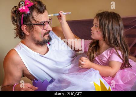 Ein Mädchen, das als Prinzessin gekleidet ist, schmückt den Vater. Spiele für Mädchen mit Papa Stockfoto