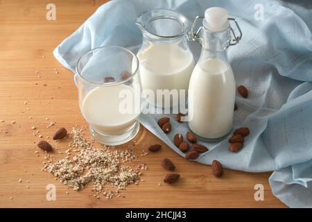 Vegane Milch aus Mandeln in Gläsern auf blauer Serviette und Holztisch, umweltfreundliche Alternative zu tierischen Milchprodukten, Kopierfläche, Stockfoto
